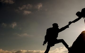 Silhouette of couple helping each other up mountain